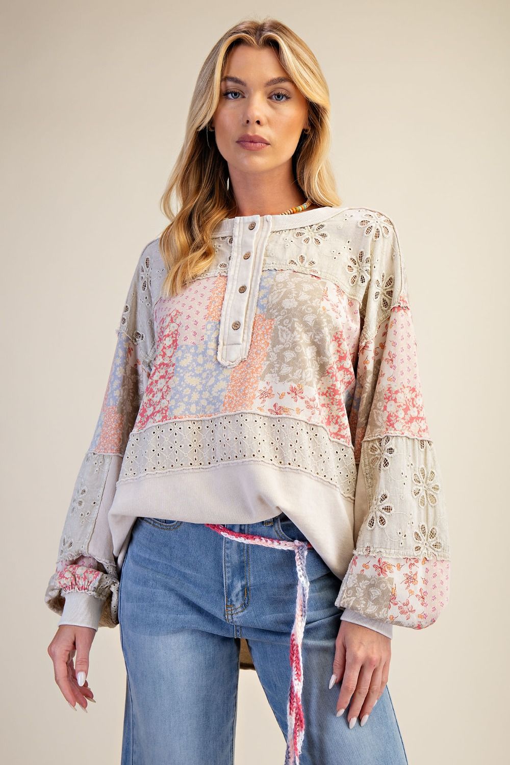 Woman wearing a floral blouse with lace details and blue jeans on a beige background