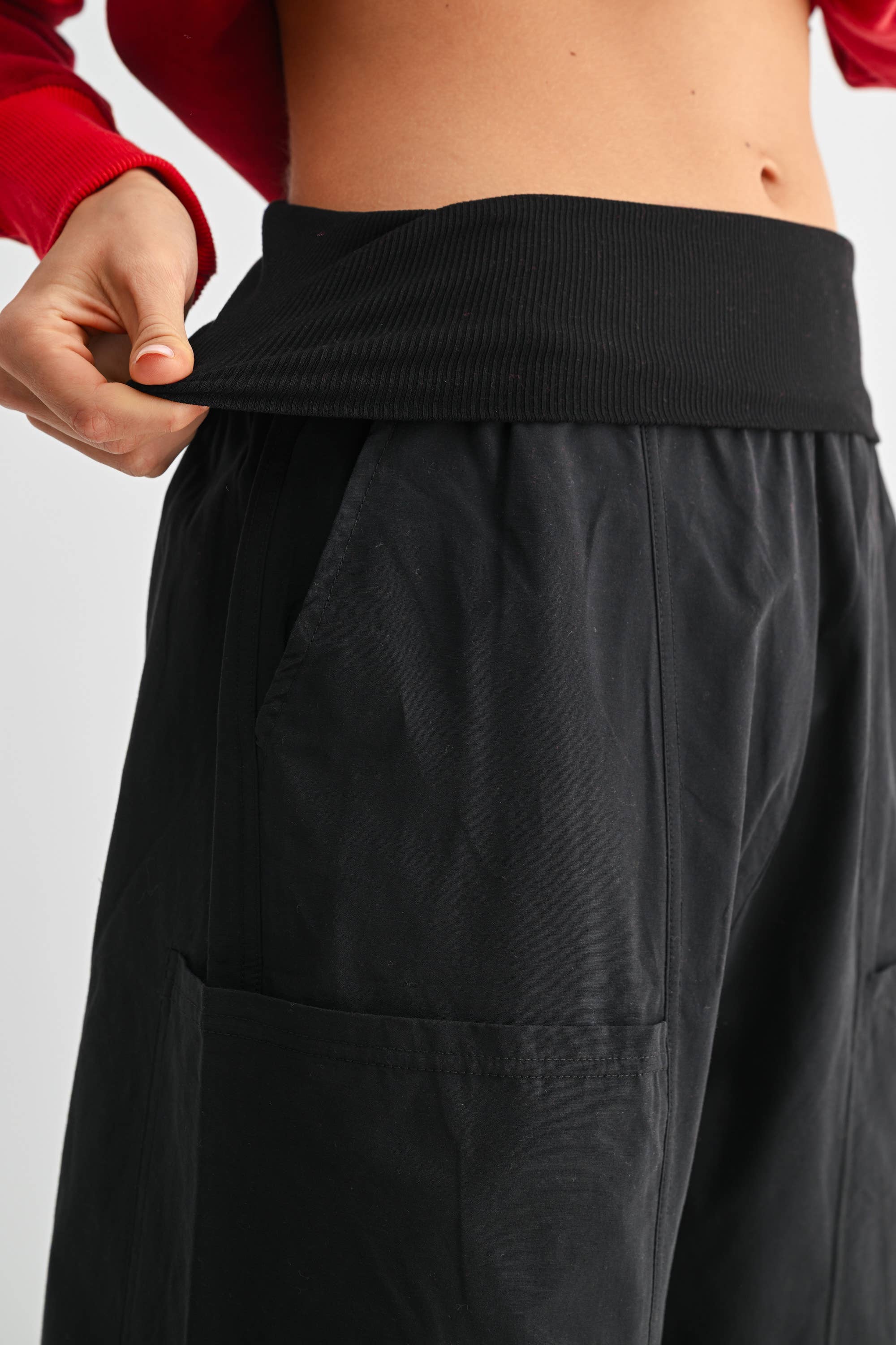 Black pants being adjusted by a person wearing a red shirt on a light gray background