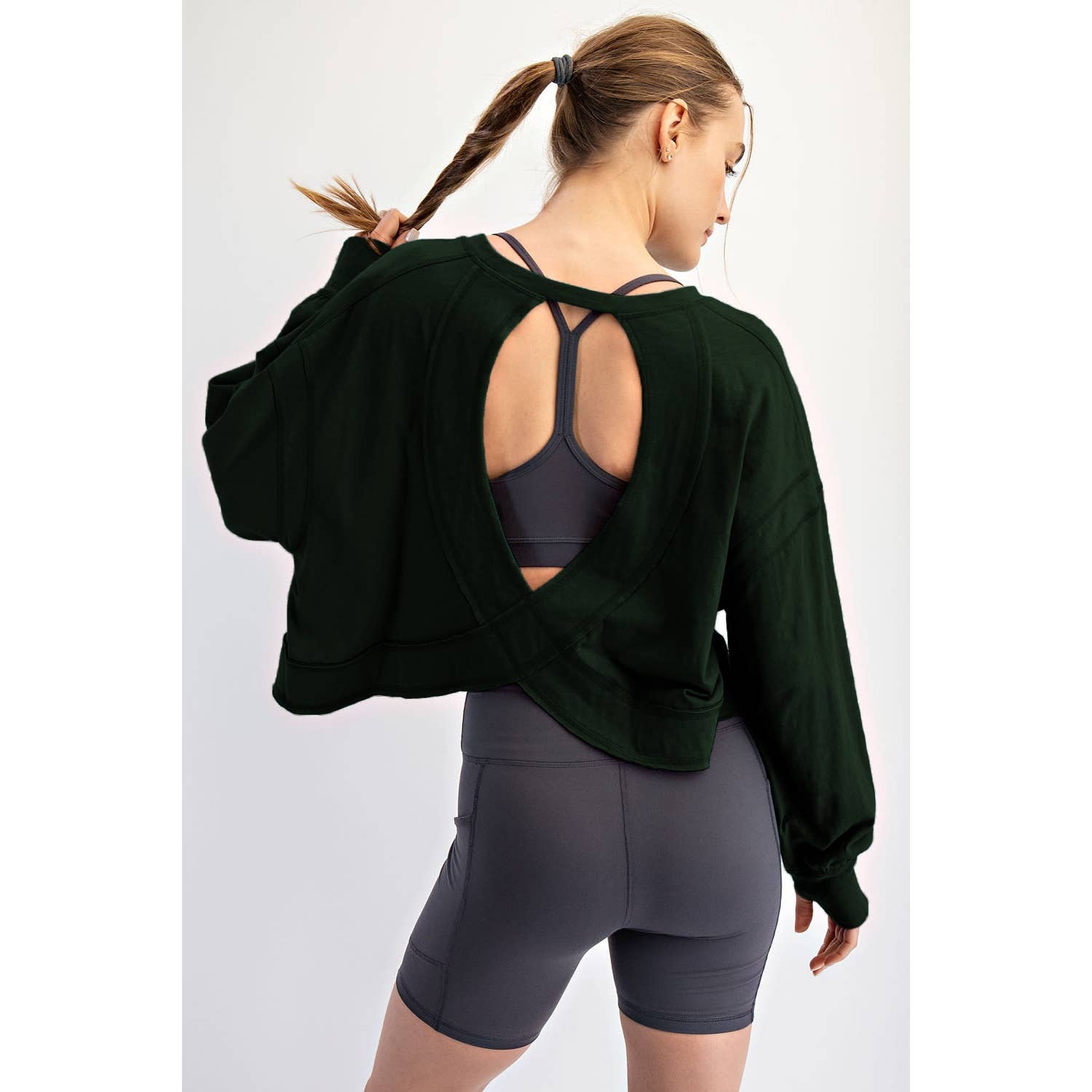 Woman wearing a green long-sleeve top with open back and gray shorts on a white background