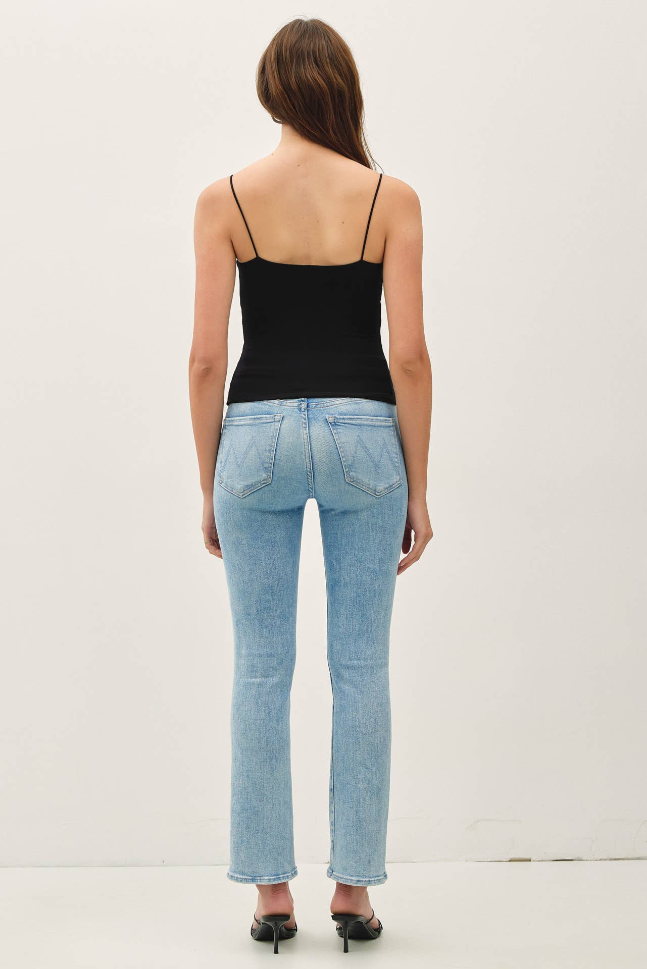 Woman wearing light blue jeans and a black top on a white background