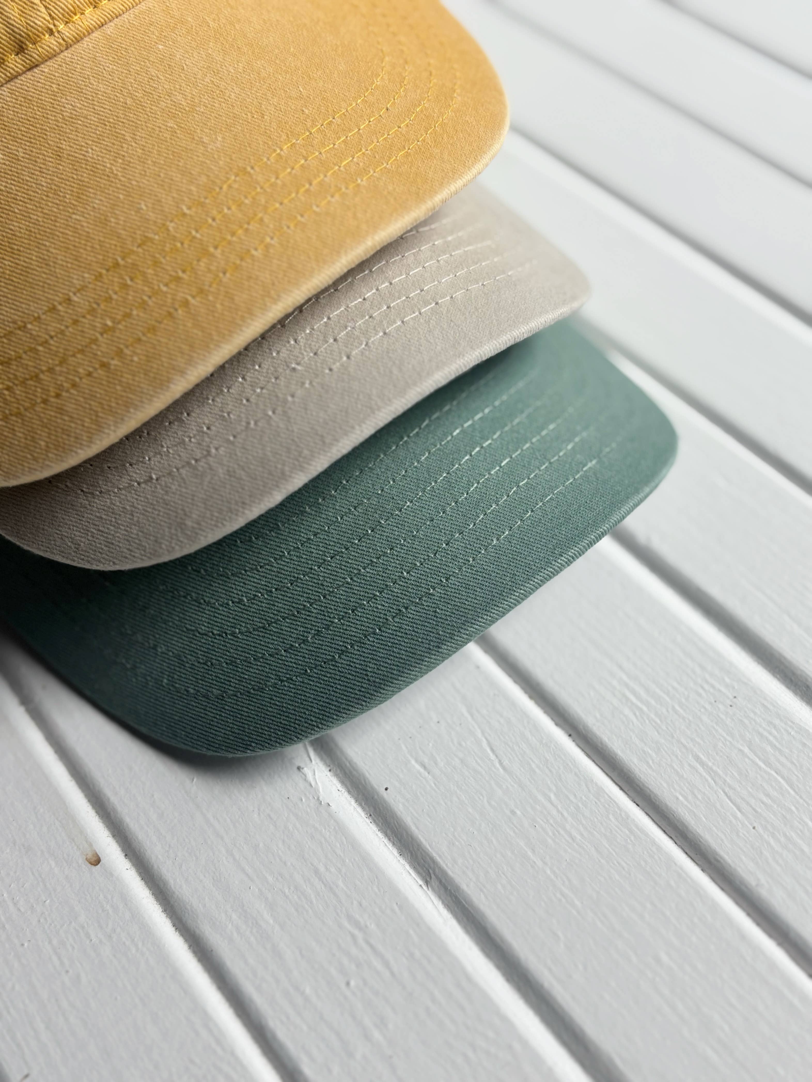 Three caps in yellow, beige, and green on a white wooden surface