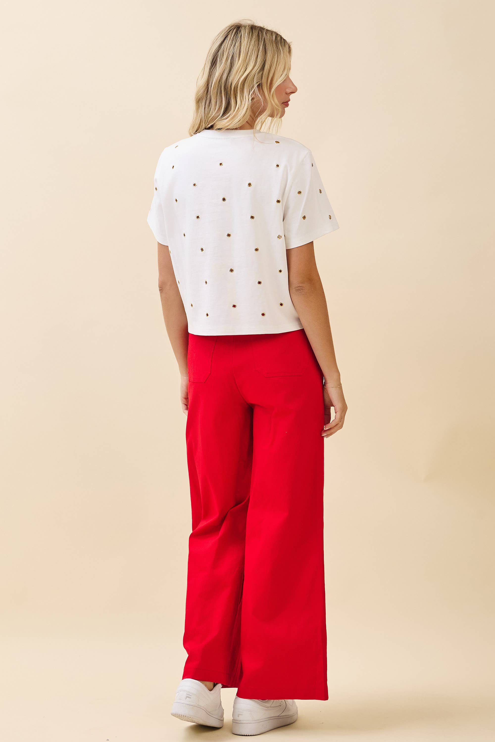 Woman wearing a white top with small black details and red pants on a beige background