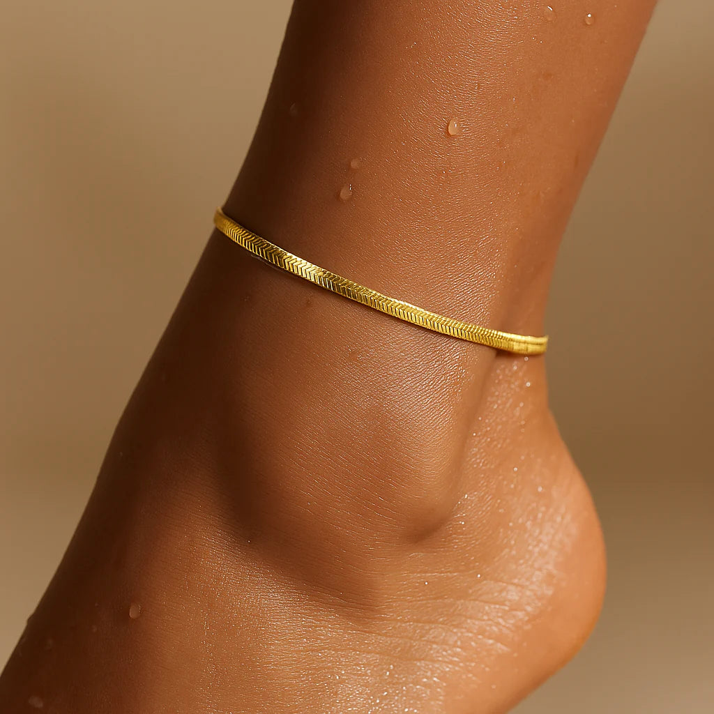 Gold anklet on a person's ankle against a beige background