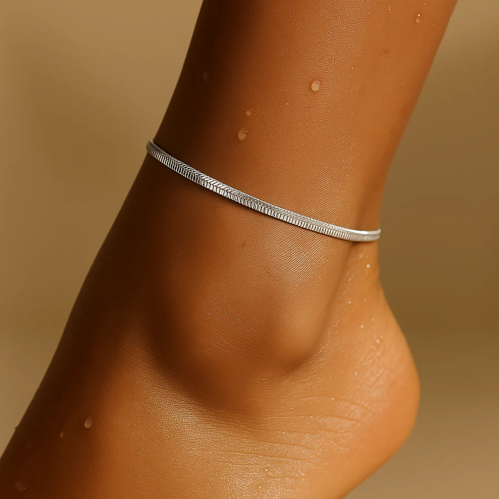 Silver anklet on a person's ankle against a beige background