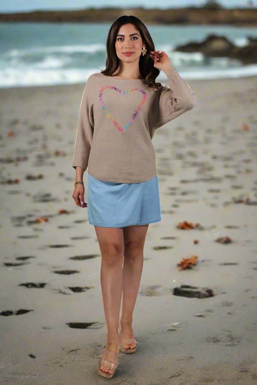 Woman wearing a beige sweater with a colorful heart design and a light blue skirt on a white background