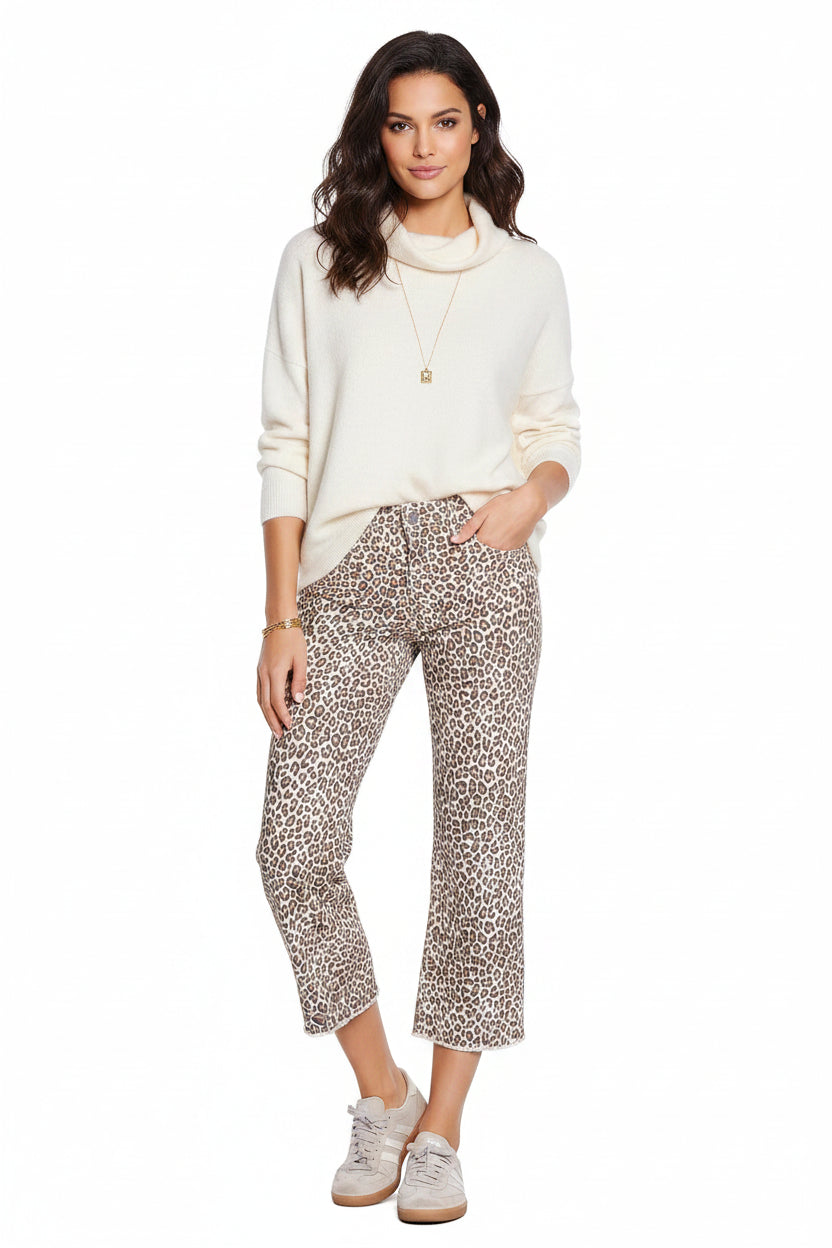 A person wearing cropped leopard-print pants with a beige base and brown/black animal spots, paired with a denim top and light sneakers, against a plain white background.